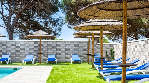 A poolside area with blue lounge chairs, thatched umbrellas, and a stone wall. - Cozy Casa Torre de Meca 1 with Pool, Terrace, and Garden (Los Caños de Meca)