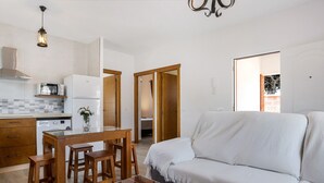 A modern kitchen with a microwave, refrigerator, wooden table, and bar stools. There is a white sofa and a glass coffee table with decorative items. - Cozy Casa Torre de Meca 1 with Pool, Terrace, and Garden (Los Caños de Meca)