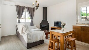 A cozy living room with a sofa, a TV, a dining table with stools, a fireplace, and a kitchen area. - Cozy Casa Torre de Meca 1 with Pool, Terrace, and Garden (Los Caños de Meca)