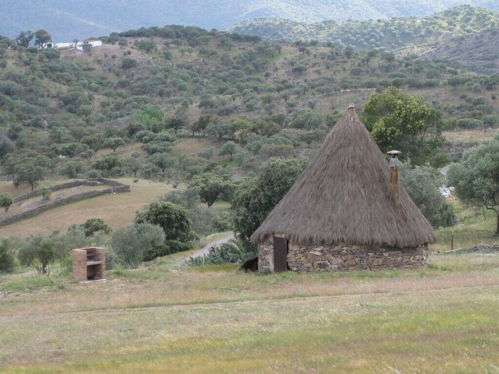 Eine strohgedeckte Hütte mit steinernen Fundamenten, eingebettet in eine hügelige Landschaft mit spärlicher Vegetation.