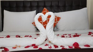 A bed with white linens, a heart-shaped towel arrangement, and scattered rose petals. - Goshen Inn Eldoret (Eldoret)