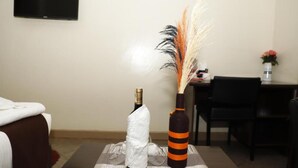 A hotel room with a bed, a small table with a bottle and a decorative vase, and a chair. - Goshen Inn Eldoret (Eldoret)