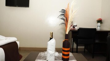 A hotel room with a bed, a small table with a bottle and a decorative vase, and a chair.