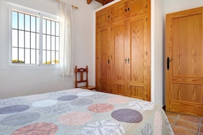 Une chambre à coucher avec un lit, une armoire en bois, une fenêtre avec des rideaux et une chaise.
