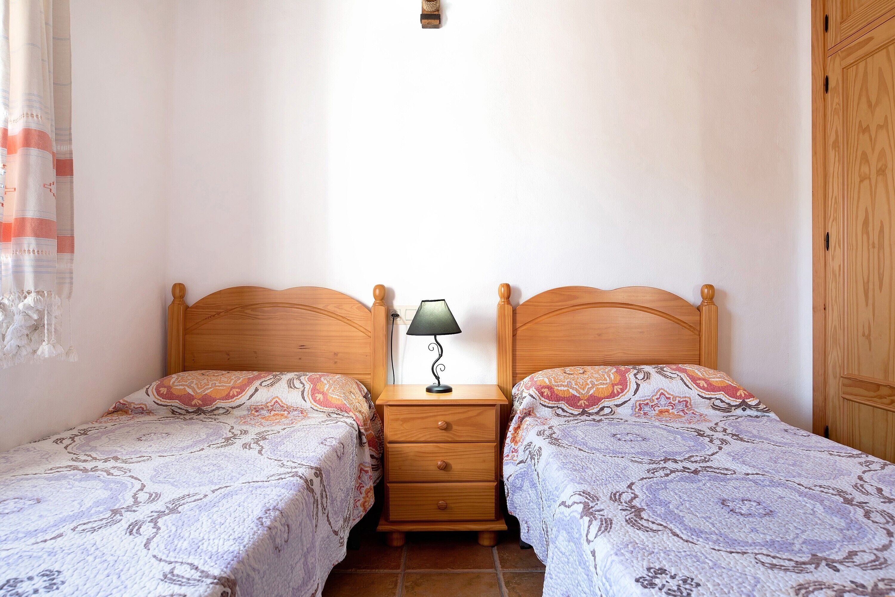 A bedroom with two single beds, a nightstand with a lamp, and a wooden wardrobe.