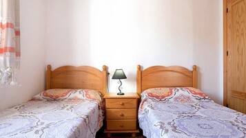A bedroom with two single beds, a nightstand with a lamp, and a wooden wardrobe.