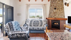 A living room with a fireplace, a sofa, and a television. - Charming Casita Torre de Meca 1 with Terrace, Garden, and Wi-Fi (Los Caños de Meca)