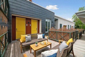 A wooden deck with outdoor seating, a yellow door, and a white building in the background.