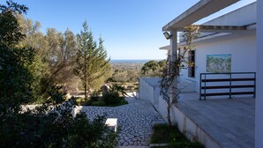 Un bâtiment moderne avec un chemin de pierre menant à une entrée blanche, entouré de verdure et offrant une vue sur un paysage lointain.