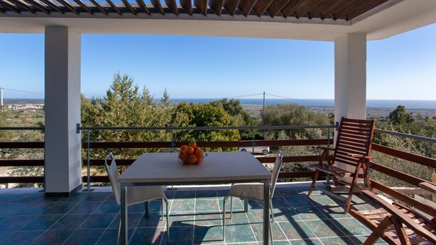 Un espace extérieur abrité, avec une table et des chaises, un saladier rempli d’oranges et une vue sur le paysage.