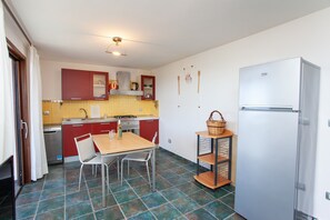 Una cocina compacta con una mesa, sillas, un refrigerador y un estante pequeño con una cesta.