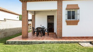 A patio with a table and chairs, a brick wall, and a window with bars. - Charming Casita Torre de Meca 2 with Terrace, Garden, and Wi-Fi (Los Caños de Meca)