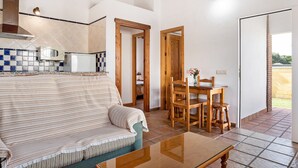 A living room with a sofa, a dining table with chairs, a kitchen area with a microwave, and a view of the outside. - Charming Casita Torre de Meca 2 with Terrace, Garden, and Wi-Fi (Los Caños de Meca)