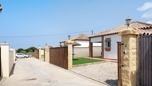 A residential street with a gated entrance, a parked car, and a house with a tiled roof. - Charming Casita Torre de Meca 2 with Terrace, Garden, and Wi-Fi (Los Caños de Meca)