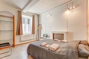 Une chambre à coucher avec un lit, un radiateur, une fenêtre avec des rideaux, une chaise et une étagère avec des cintres.