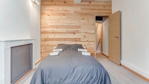 A bedroom with a bed, a wooden wall panel, a door, and a small window.