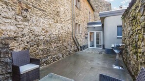 A stone-walled courtyard with wicker furniture and a glass table.