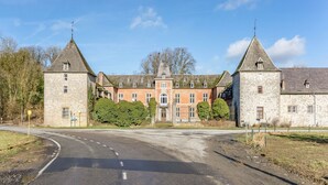 A large stone building with two towers, a central entrance, and a paved driveway.