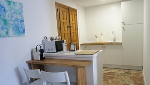 Una cucina compatta con forno a microonde, bollitore e un armadietto in legno. Sono presenti due sedie bianche e un piccolo tavolo.