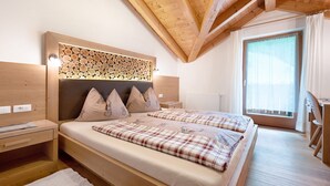 Une chambre à coucher en bois, avec un lit, des tables de chevet, une tête de lit ornée d’un motif imitant des troncs d’arbres, et une fenêtre avec des rideaux.