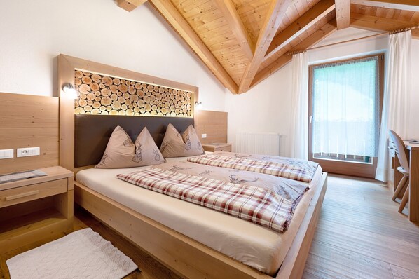Une chambre à coucher en bois, avec un lit, des tables de chevet, une tête de lit ornée d’un motif imitant des troncs d’arbres, et une fenêtre avec des rideaux.