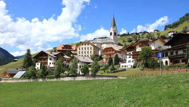 Un village perché sur une colline, avec ses maisons traditionnelles en bois, une église et un ciel d’un bleu éclatant.