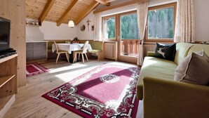 Une pièce chaleureuse avec un plafond en bois, une table à manger, un canapé et une grande fenêtre donnant sur les arbres.