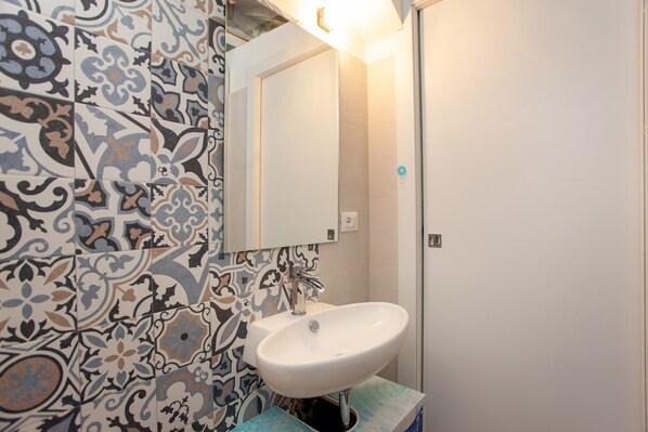Un baño con baldosas estampadas, un lavabo blanco y un espejo.
