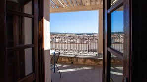 Eine offene Holztür führt zu einem Balkon mit Metallgeländer, einem Stuhl und freiem Blick auf die Stadtlandschaft.