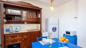 Eine kompakte Küche mit Holzschränken, einem weißen Kühlschrank, einer Mikrowelle und einem Esstisch mit blauer Tischdecke.