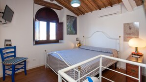 Ein Schlafzimmer mit Bett, Stuhl, Schreibtisch, Fernseher und Fenster.
