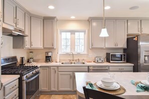A modern kitchen with a stove, microwave, sink, and dining area. - Heated Saltwater Pool Hot Tub! (Eastham)