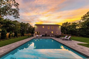 A rectangular swimming pool with a patio area, lounge chairs, and a building with a flat roof in the background. - Heated Saltwater Pool Hot Tub! (Eastham)