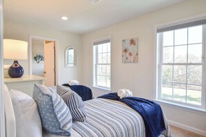 A bedroom with two beds, a lamp, artwork, and large windows. - Heated Saltwater Pool Hot Tub! (Eastham)