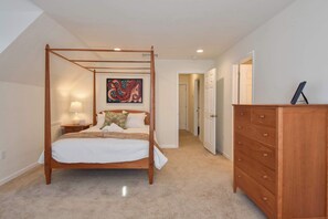 A bedroom with a four-poster bed, a nightstand with a lamp, a dresser, and a painting on the wall. - Heated Saltwater Pool Hot Tub! (Eastham)