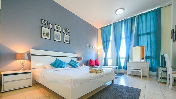 A modern bedroom with a large bed, bedside tables, a desk, and a chair. - SND - Bright and Spacious Studio (Dubai)