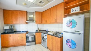 A kitchen with wooden cabinets, a stove, a washing machine, and a refrigerator with stickers. - SND - Bright and Spacious Studio (Dubai)