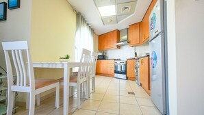 A kitchen with wooden cabinets, a white refrigerator, and a dining table with chairs. - SND - Bright and Spacious Studio (Dubai)