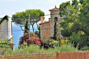 A coastal building with a stone tower, surrounded by greenery and a clear view of the sea. - Beautiful Villa "Es Pas" with Pool, Air Conditioning, Wi-Fi, Terraces & Ocean Views (CALA PI)