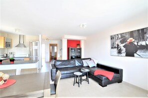 A modern living room with a black leather sofa, a dining table with chairs, a kitchen area, and a red accent wall. - Beautiful Villa "Es Pas" with Pool, Air Conditioning, Wi-Fi, Terraces & Ocean Views (CALA PI)