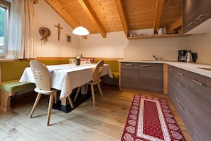 A cozy dining area with a table, chairs, and a bench. A kitchen with cabinets and a sink is visible in the background.