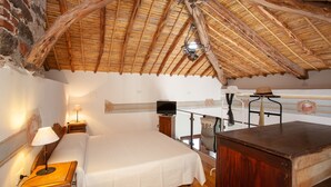 Quarto com cama, escrivaninha, televisão e varanda com grade de madeira.