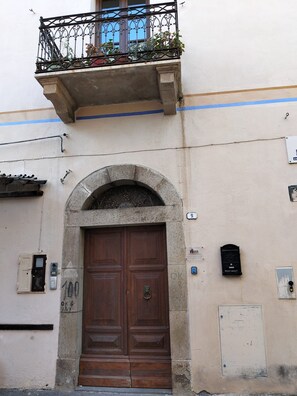 A building facade with a large wooden door, an arched entrance, a balcony with metal railing, and a small mailbox. - Apartment "Hora Est" with Sea View, Terrace, Wi-Fi, and Private Parking (Orosei)