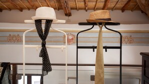 Quarto com teto alto e vigas de madeira, parede branca com desenhos decorativos e dois chapéus em um suporte.