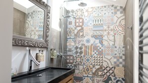 Une salle de bain avec un lavabo à vasque et un plan de toilette noir, un miroir doté d’un cadre orné et une douche aux carreaux décoratifs.
