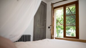 Une chambre à coucher avec un lit, une porte en bois et une fenêtre donnant sur un paysage verdoyant.