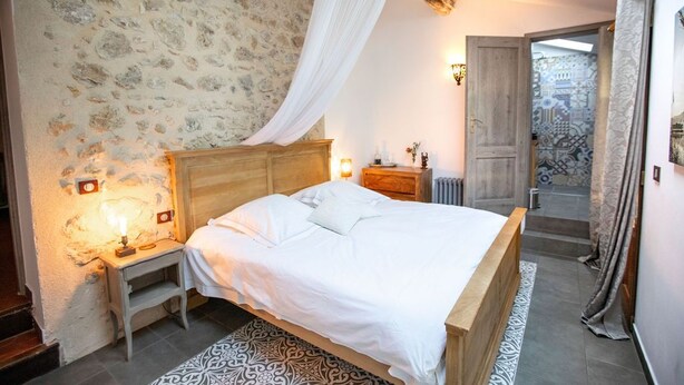 Une chambre avec un mur en pierre, un cadre de lit en bois, une table de chevet, une lampe de chevet et un tapis à motifs.