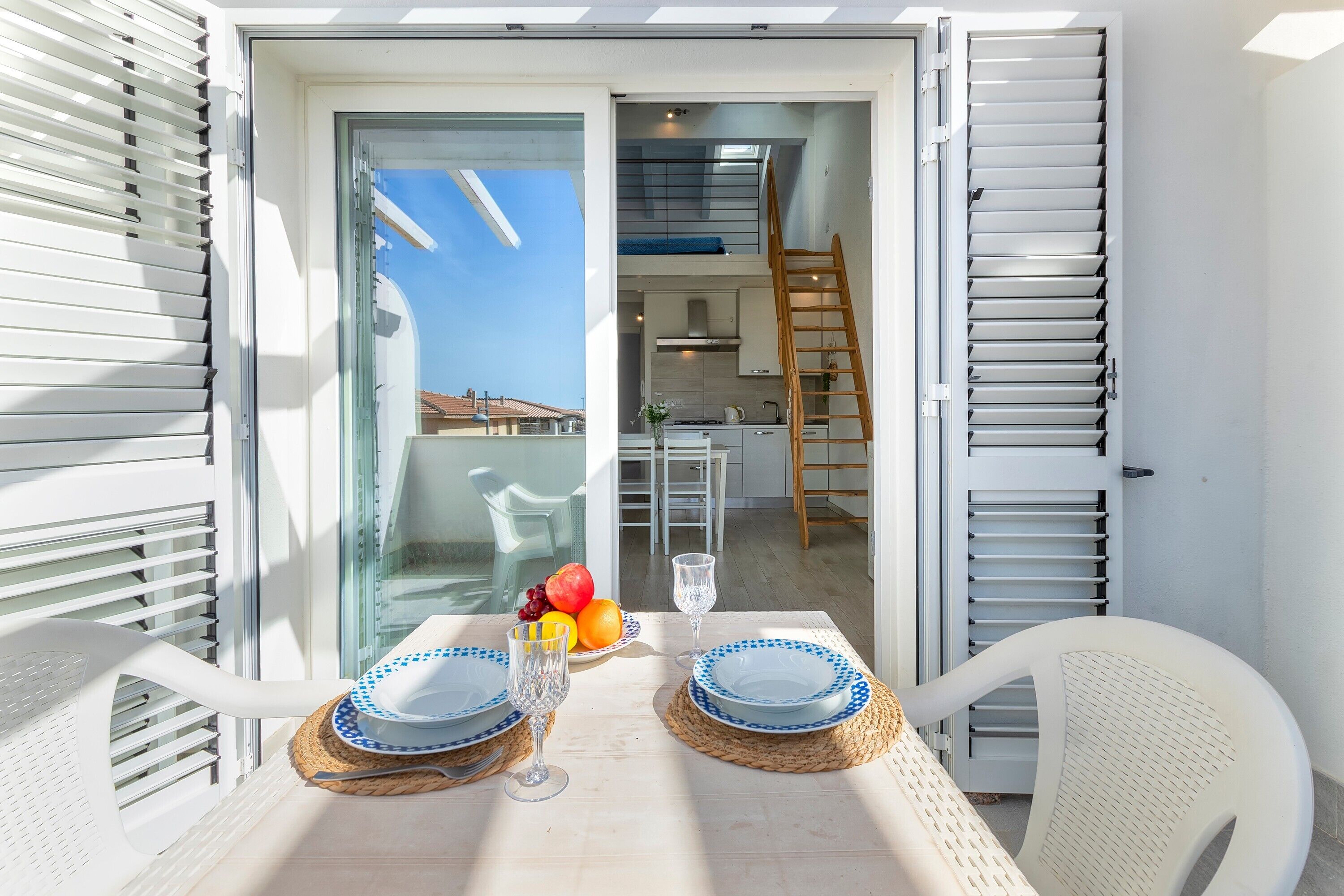 Un balcon avec une table dressée pour deux personnes, une cuisine en arrière-plan et une vue sur le ciel.