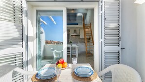 Varanda com mesa posta para dois, cozinha ao fundo e vista do céu.