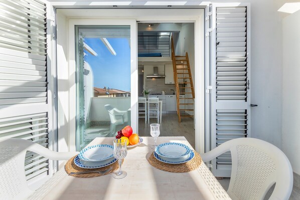 Un balcón con una mesa para dos, una cocina al fondo y vista al cielo.
